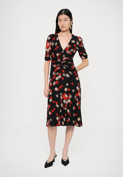 Musta mekko, jossa punaisia ja beigejä pilkkuja, lyhyet hihat, V-aukko, rypytetty etuosa, liehkuva helma, sileä pinta, yhdistetty mustiin korkokenkiin.