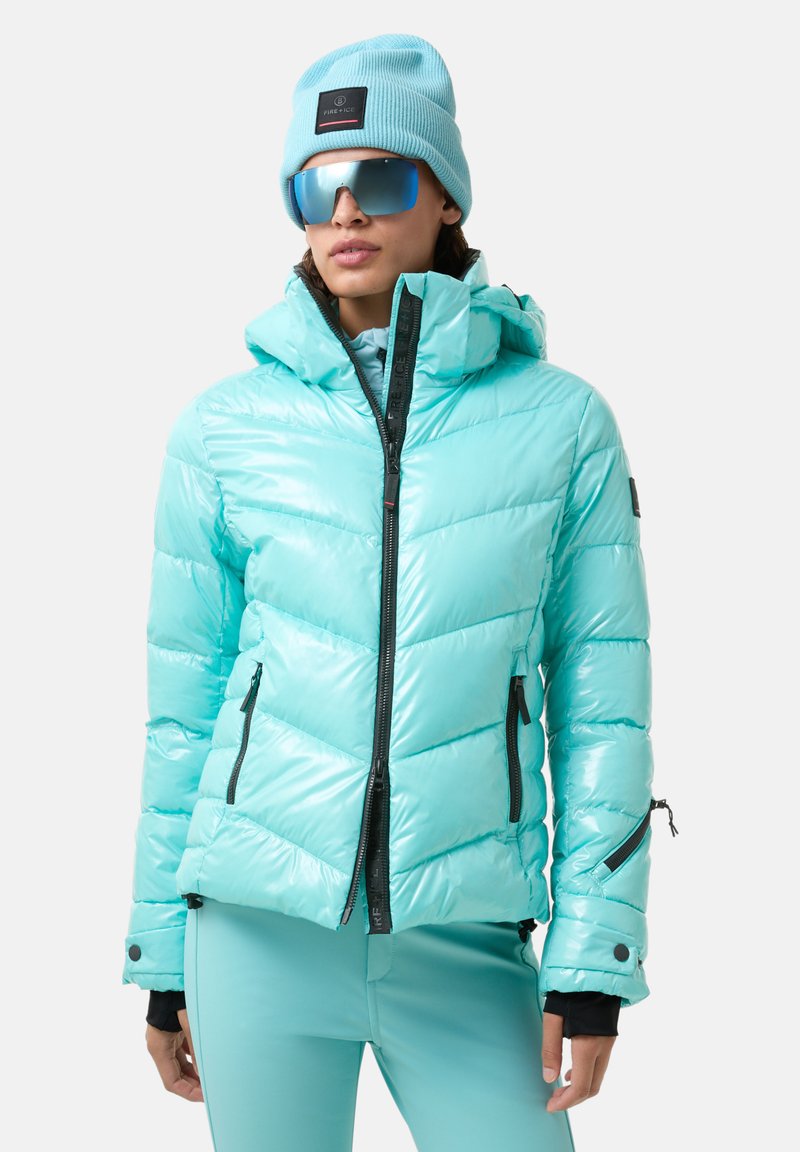 Turquoise donsjack met capuchon, voorzien van chevronstiksels, zwarte ritsen en een gladde, glanzende textuur. Gecombineerd met bijpassende broek.