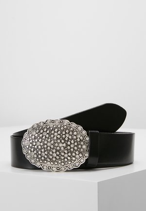 Ceinture en cuir noir avec grande boucle ovale en argent avec des détails en relief de perles circulaires, présentée enroulée sur une surface blanche.