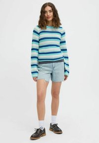 Randig stickad tröja i blå och gröna nyanser, ihopparad med ljusa denimshorts. Anmärkningsvärda detaljer inkluderar långa ärmar och en avslappnad passform.