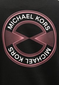 Μαύρο ύφασμα με κυκλικό γραφικό που περιλαμβάνει ροζ σχέδιο. Το κείμενο αναγράφει «MICHAEL KORS» με λευκά γράμματα, περιβάλλοντας ένα διασταυρούμενο μοτίβο.