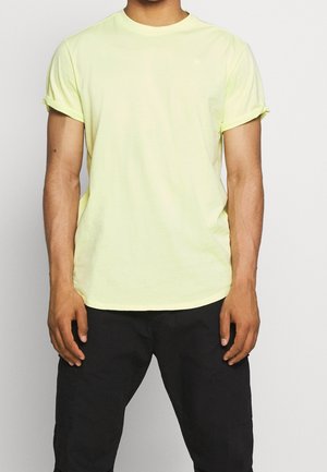 Neon żółta bawełniana koszulka z podwiniętymi rękawami, okrągłym dekoltem i luźnym fasonem. W połączeniu z ciemnymi spodniami. Minimalne zdobienia.