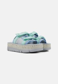 Des sandales bleu clair et vert menthe avec une semelle plate-forme blanche épaisse tachetée et des sangles réglables, présentées sur un fond blanc.