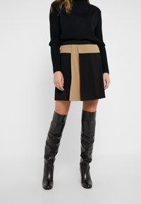 Zwart en tan kleur geblokt mini-jurkje met een tailormade pasvorm, gemaakt van een soepele stof. Gecombineerd met strakke zwarte leren kniehoog laarzen.