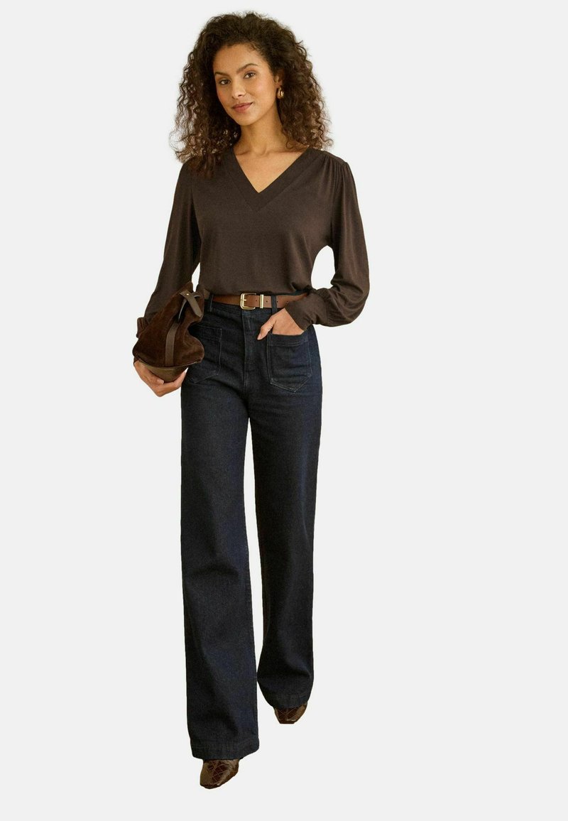 Pruun pika varrukaga pusa V-kaelusega, kombineeritud kõrge vöökohaga tume teksariidest laia lõikega pükstega ja pruunide kontsakingadega. Käes pruun käekott.