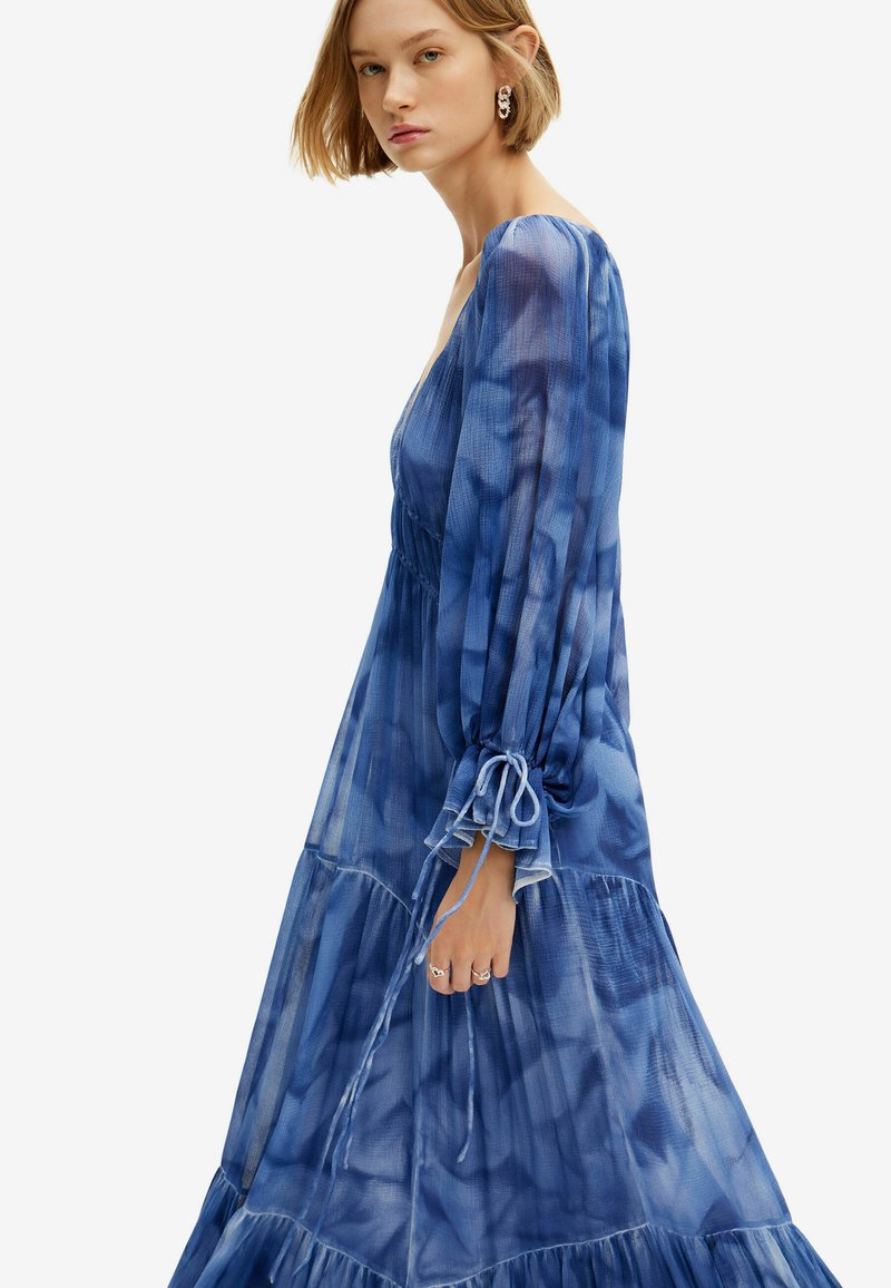 Maxikleid in Blau mit Batikmuster, langen Ballonärmeln, gestuften Rüschen und Kordelzugdetails an den Bündchen. Durchsichtige, leichte Textur.