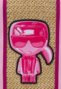 Slámový sáček s lesklou růžovou postavou v brýlích, oblečenou v růžovém oblečení. Akcenty v růžové barvě, na texturovaném slámovém pozadí.