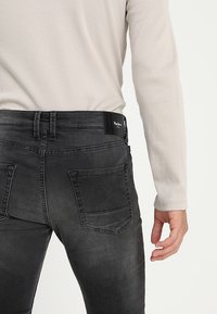 Jeans de mezclilla negro con un ajuste slim, que presentan una textura suave, bolsillos traseros y una etiqueta de cuero negro con marca en la cintura.