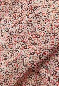Tissu léger avec un petit motif floral irrégulier dans des tons marron, rouge et rose, montrant une couture et des plis superposés.