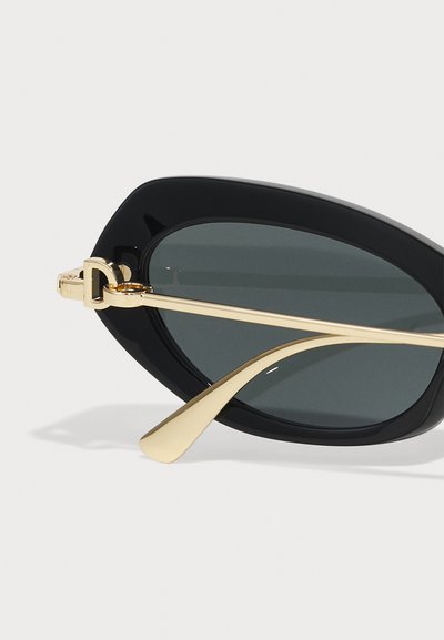 Black oversized sunglasses with gold-tone metal accents. Features flat lenses and sleek, smooth frames with defined edges.