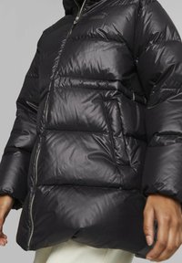 Černá péřová bunda s lesklým povrchem, zapínáním na zip a oversized siluetou s bočními kapsami a prošívanými částmi.