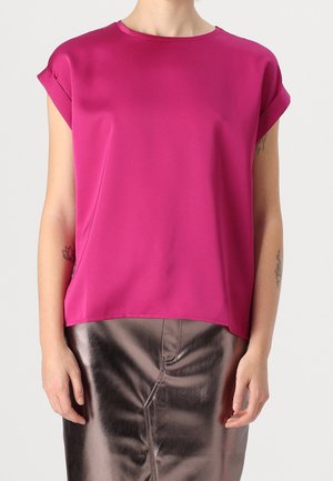 Osoba ubrana w magentowy top z krótkim rękawem i mankietami oraz błyszczącą brązową spódnicę z wysokim stanem, stojąca na jednolitym tle.