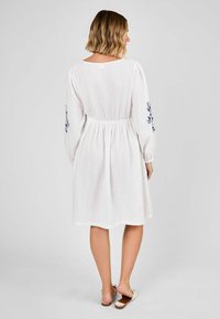 Weißes, weit geschnittenes Kleid mit langen, gepufften Ärmeln, elastischem Bund und blauer floraler Stickerei an den Ärmeln. Strukturierter Stoff. Lässige Länge.