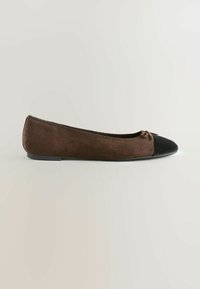 Braune Wildleder-Ballettschuhe mit schwarzem Zehenkappe und kleiner dekorativer Schleife, seitlich auf einem schlichten hellen Hintergrund betrachtet.
