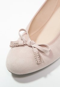 Ballet flats en suède rose clair avec un bout arrondi, un nœud décoratif et des glands avec de petites rivets en façade. Doublure intérieure douce.
