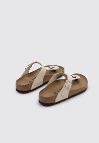 Sandali Birkenstock con cinturini sintetici beige, soletta in sughero e suole in gomma nera. Caratterizzati da fibbia regolabile e design con cinturino per le dita.