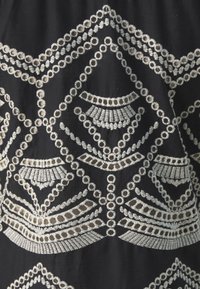 Tessuto nero con intricate ricami bianchi in motivi geometrici, con dettagli circolari e lineari, creando un aspetto testurizzato.