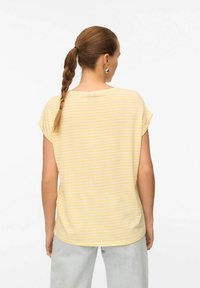 Geel gestreept t-shirt met korte mouwen, ronde halslijn en een iets losse pasvorm. Gepaard met lichtgrijze broek. Glad textuur.