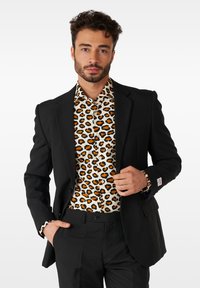 Črni tailoring blazer preko bele srajce z oranžno-črnimi leopardjimi potiski. Srajca ima ovratnik s gumbi in usklajene manšete.