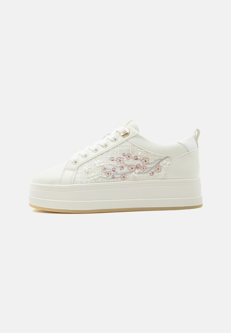 Witte platformsneaker met een paneel van kant met roze bloemenborduursel en kralen, vetersluiting en een lus aan de hiel.