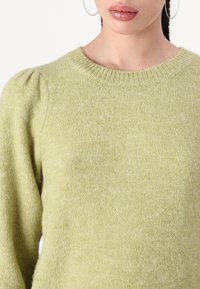 Lys grønn strikket genser med rund hals, textured stoff og puffermansjetter. Myk, varm utseende.