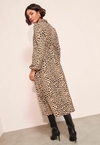 Lapsuļa raksta vidēja garuma kleita ar pūkainām piedurknēm. Audums ir gluds, ar melniem plankumiem uz brūngana fona. Kombinēta ar augstiem melniem zābakiem.