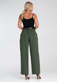 Czarny dopasowany top na ramiączkach w połączeniu z luźnymi, oliwkowymi spodniami z wysokim stanem. Spodnie mają pasek w talii i boczne kieszenie.