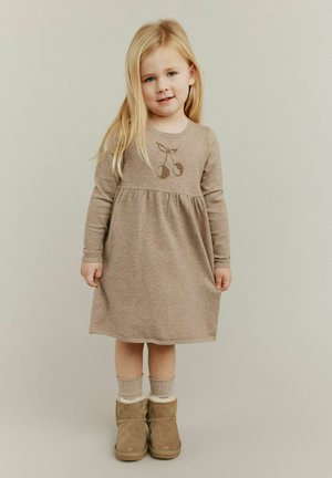 Brązowa dzianinowa sukienka z długimi rękawami i marszczonym pasem, z motywem wiśni. W połączeniu z beżowymi butami z futrem oraz jasnymi skarpetkami.