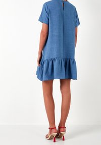 Modré šaty po kolena s krátkými rukávy, řaseným lemem a výřeze na zádech ve tvaru klíče. Vyrobeno z texturované látky.