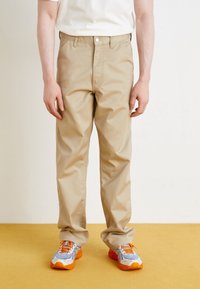 Beige chinos with a straight-leg fit, featuring a button closure and side pockets. Paired with colorful athletic shoes in blue and orange.
