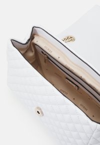 Borsa a tracolla bianca trapuntata con una texture liscia, hardware dorato e un interno beige che presenta una tasca con zip. Logo stampato sulla fodera.
