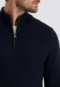 Marineblauer Strickpullover mit hohem Kragen, ausgestattet mit einem Reißverschluss am Hals und einem strukturierten Zickzackmuster auf der Vorderseite.