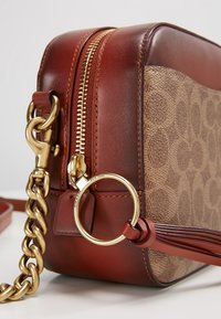 Ruskea nahkainen ja kangasinen olkalaukku, jossa vetoketjusuljin, kullanväriset metalliosat, ketjuhihna ja sivulla teksturoitu logokuvio.