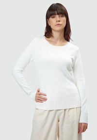 Weißer Pullover mit langen Ärmeln aus weichem Material, mit Rundhalsausschnitt und gerippten Bündchen sowie Saum. Getragen mit hellen, locker sitzenden Hosen.