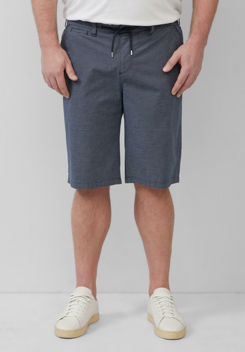 Shorts à carreaux bleu foncé avec un cordon de serrage à la taille et deux poches avant, assortis à des baskets blanches et un t-shirt blanc uni.