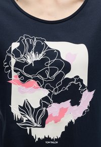 Μπλε ναυτικό πουκάμισο με λευκό, ροζ και ανοιχτό μοβ αφηρημένο λουλουδένιο σχέδιο και το κείμενο «Tom Tailor» στο κάτω κέντρο.