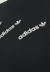 Black cotton t-shirt with white Adidas logo and trefoil accents. Features short sleeves and a rounded neckline, smooth texture.