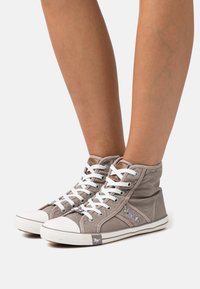 Sapatilhas de lona de cano alto em cinza claro com atacadores brancos, biqueira de borracha branca em contraste e detalhes em couro castanho na língua.