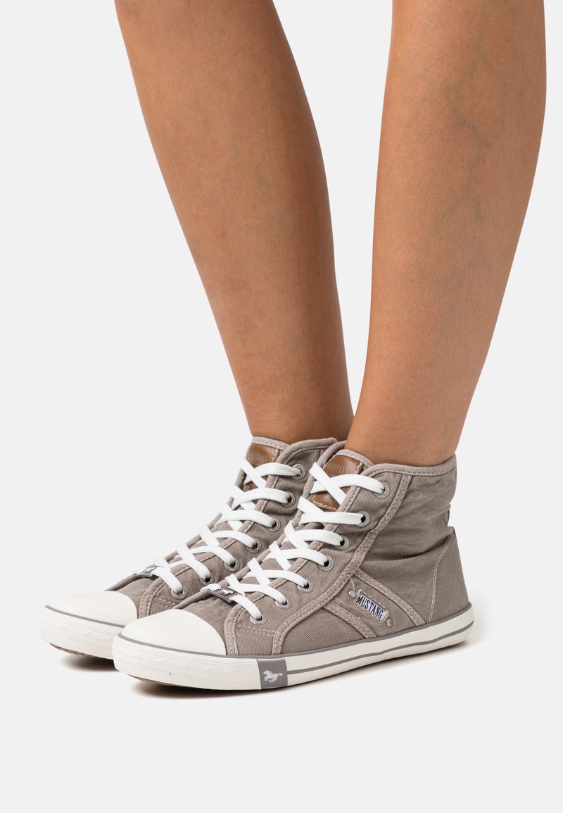 Sapatilhas de lona de cano alto em cinza claro com atacadores brancos, biqueira de borracha branca em contraste e detalhes em couro castanho na língua.