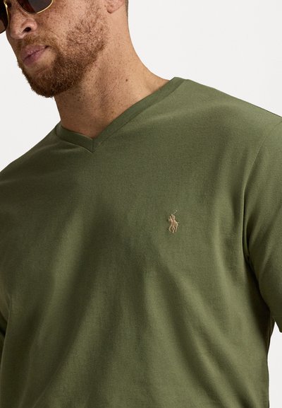 T-shirt w kolorze oliwkowym z dekoltem w serek, wykonany z miękkiej bawełny. Posiada małe haftowane logo na lewej piersi. Gładka struktura, luźny krój.