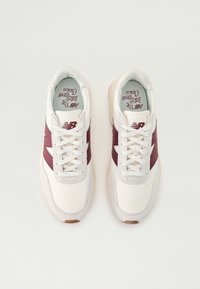 Baskets de sport blanches avec des accents maron foncé, en matériaux en mesh et cuir, à bout rond et lacets plats. Le texte sur la semelle intérieure indique "Le choix intelligent."