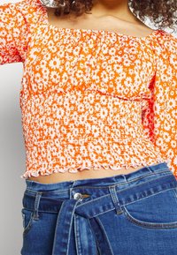 Top con stampa floreale arancione, design smock, maniche lunghe e orlo scallop, abbinato a jeans in denim blu a vita alta.