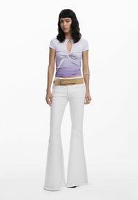 Top ajustado en ombré lila con un corte en forma de llave, combinado con jeans acampanados blancos con bordes desflecados y un cinturón marrón con detalles de hebilla metálica.