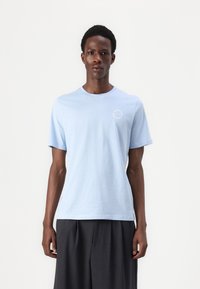 Light blue cotton T-shirt with a crew neckline, short sleeves, and a small circular logo on the left chest.