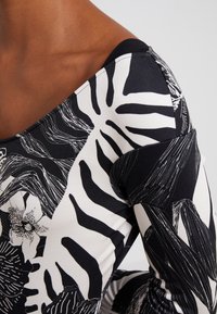 Långärmad topp med ett svart och vitt mönster av blommor och zebrarand. Tillverkad av mjukt tyg med en åtsittande silhuett och bred halsringning.