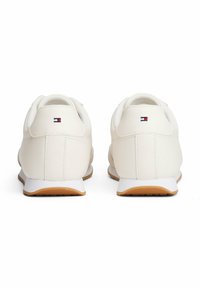 Un paio di sneakers bianche casual con suole di gomma, viste da dietro, con un piccolo logo rosso, bianco e blu su ciascun tallone.