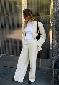 Krēmkrāsas bleizeris un saskaņotas platas bikses, apvienotas ar pieguļošu baltu topu. Melna rokassoma, saulesbrilles un gludas tekstūras.