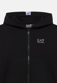 Sudadera con capucha negra con cremallera, hecha de material suave. Cuenta con un bolsillo frontal, un sutil logo EA7 y un acento gris en el borde de la capucha.