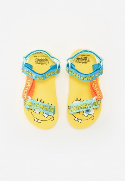 Gele sandalen met een SpongeBob SquarePants ontwerp. Voorzien van blauwe en oranje verstelbare riemen met de tekst "IMAGINAATION" en een gestructureerde zool.