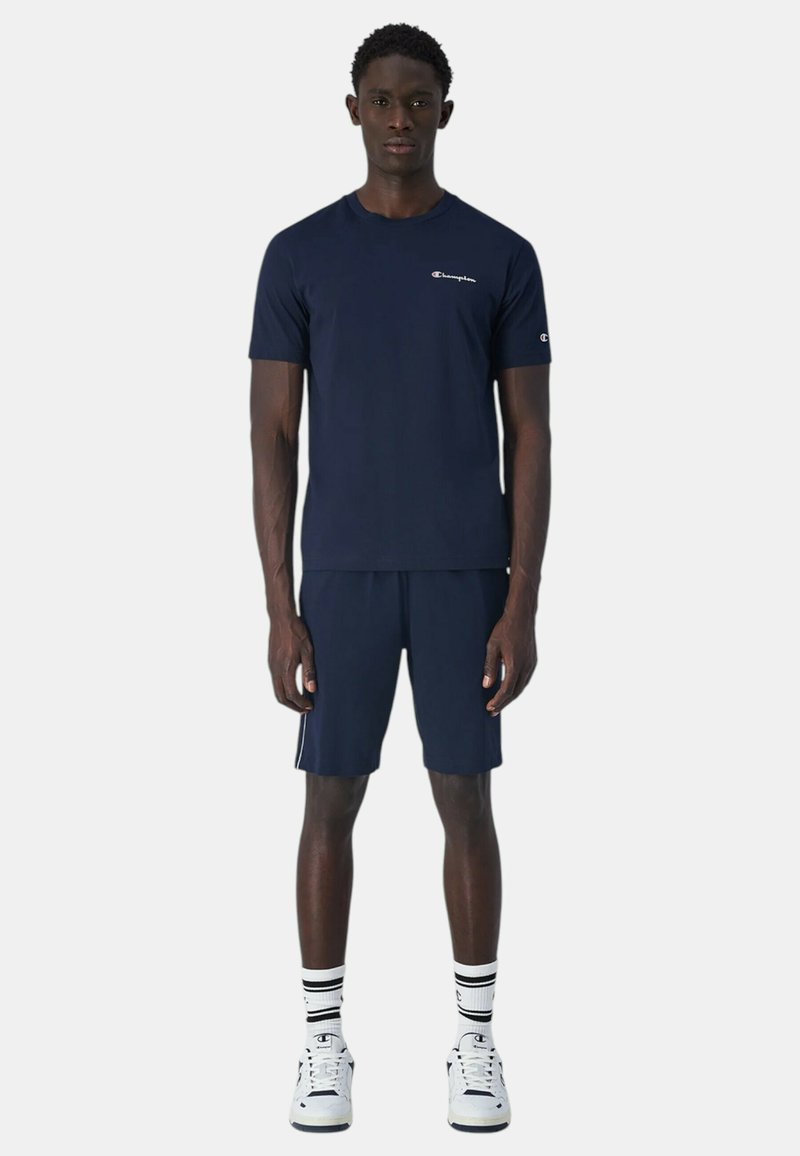 Camiseta atlética de manga corta en color navy con un pequeño logo en el pecho, combinada con pantalones cortos a juego. Incluye calcetines con rayas blancas y zapatillas.